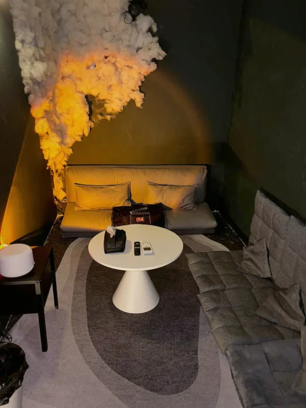 Cozy storm-themed movie room with a cloud-like installation over a mustard sofa, dark walls, and a modern white coffee table.