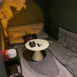 Cozy private movie room at Rochor with a fluffy cloud installation above a mustard sofa, surrounded by dark walls and modern decor.